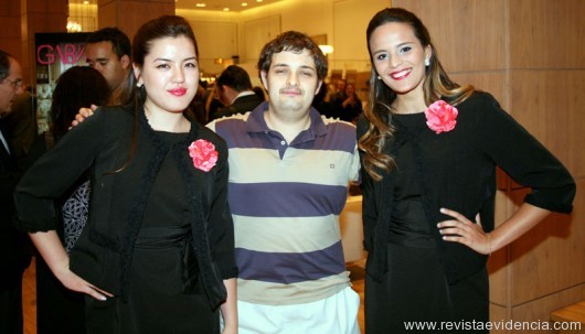 O conferencista Paulo Kogos emoldurado pelas recepcionistas do evento, Lais Harumy e Bruna Serrano